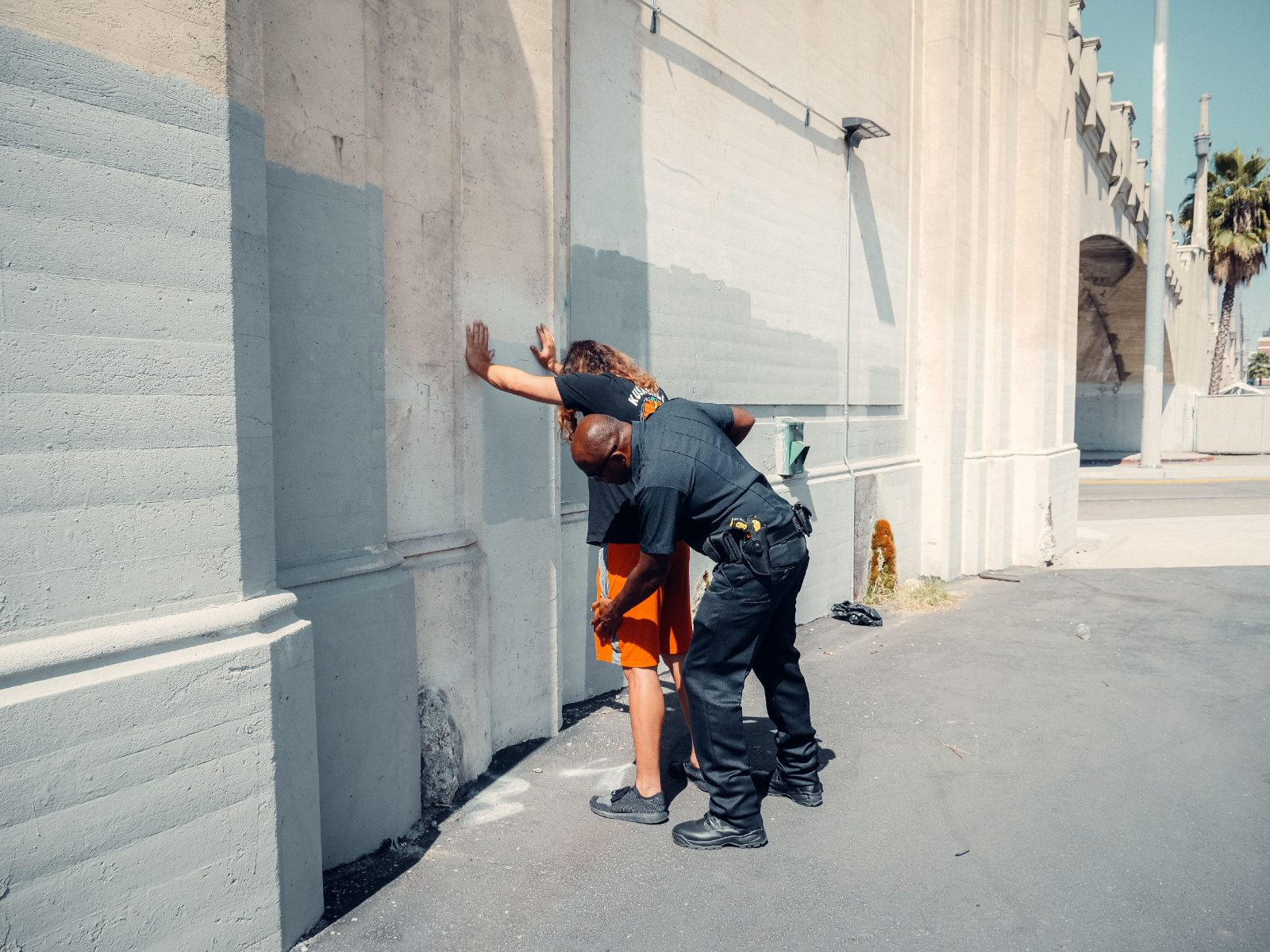 A police officer conducts a pat down search on a suspect outdoors near a wall, showcasing law enforcement procedures.