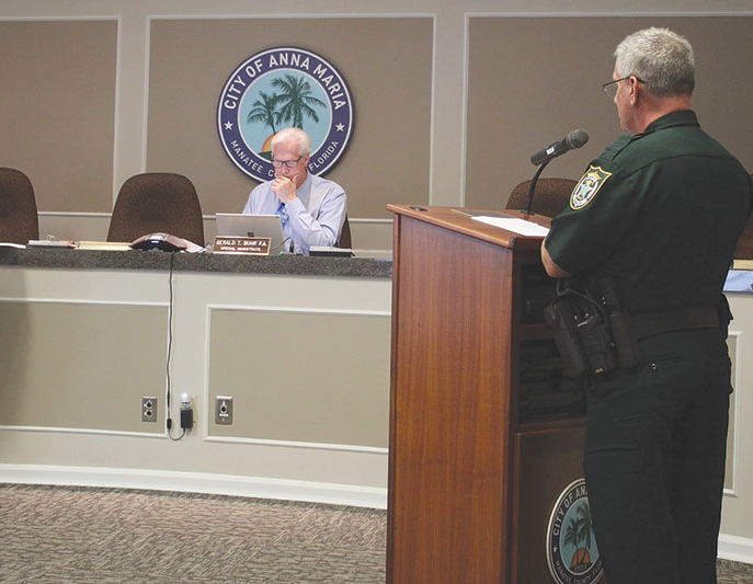 Special magistrate presiding over a City of Anna Maria code enforcement hearing, with a uniformed officer at the podium.